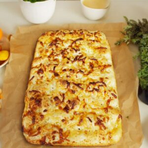 Cheese flatbread on parchment with herbs nearby.