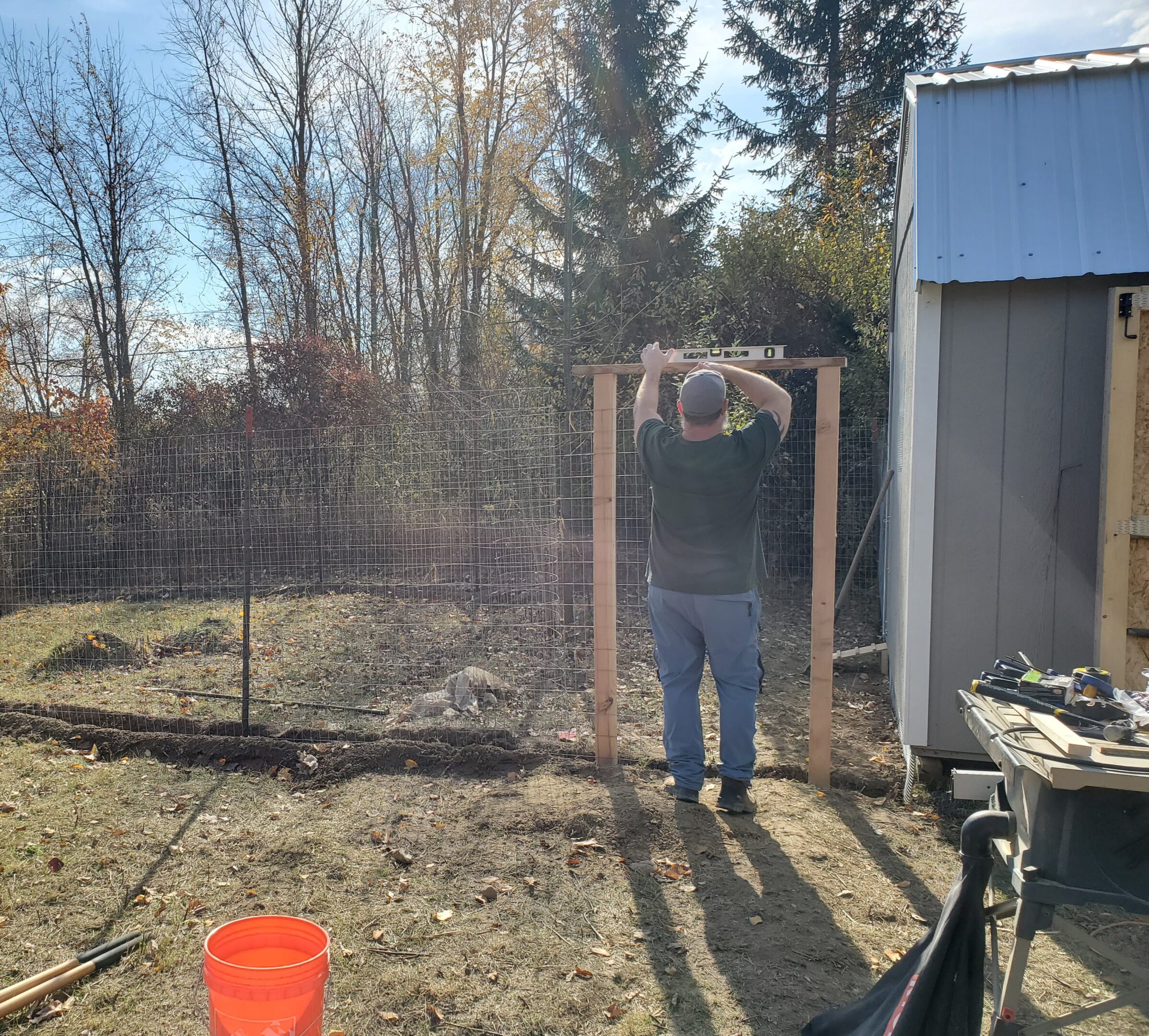 Man building fence next to small shed.